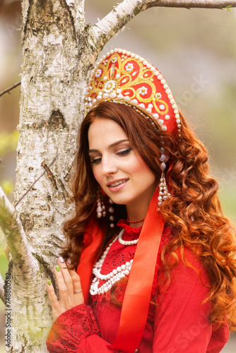 russian girl in traditional russian sarafan and kokoshnik embroidering outdoors photo