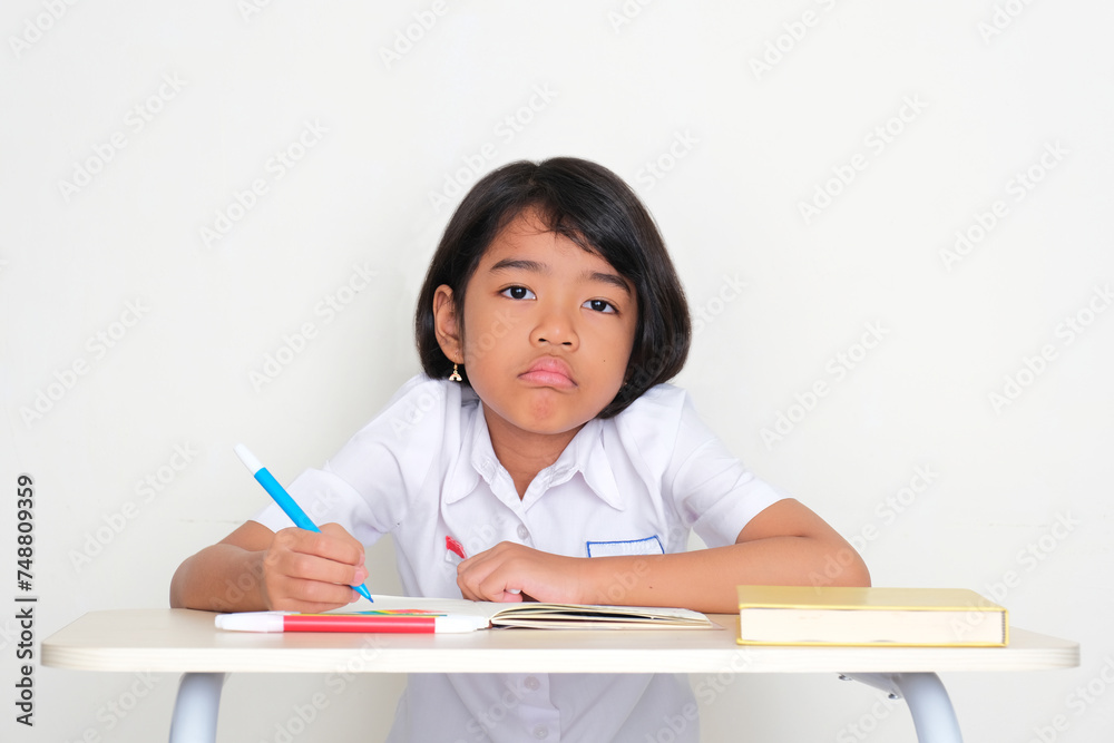Indonesia kid student sitting on school desk with sad expression Indonesia kid student sitting on school desk with sad expression