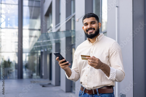 Young man using a smartphone and holding a credit card on a city street