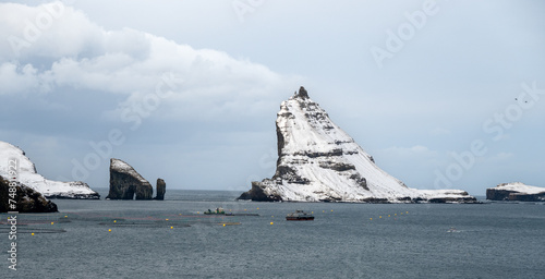 Rock Tindholmur with snow near Vagar, Faroe Islands
and the two rocks Drangarnir. 
Fish farm in the foreground photo