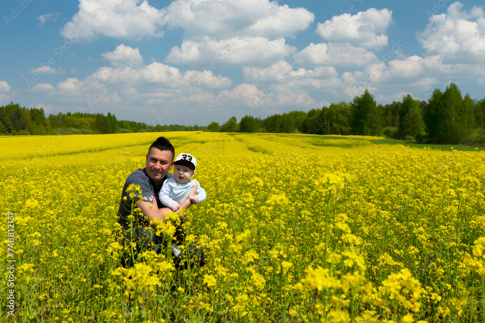 Handsome dark-haired man, dad holds his little son in his arms in a rapeseed field. Copy space.
