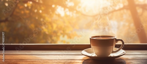 A cup of coffee is placed on top of a wooden table, by a window where sunlight is streaming in. It seems to be a relaxing moment of a morning coffee break.