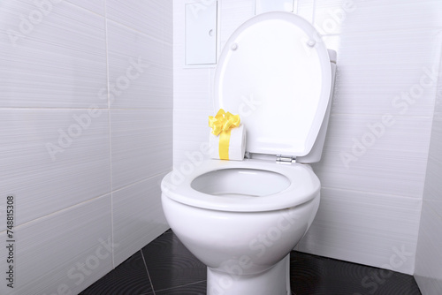 White home toilet with flush and white toilet paper with a gift yellow bow in the bathroom. Quarantine concept.