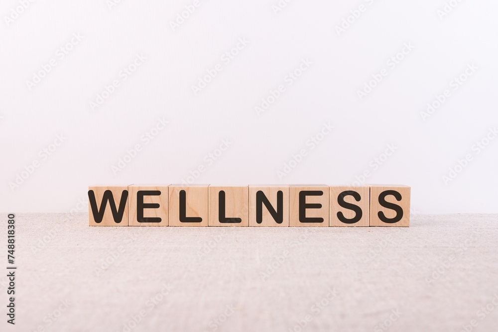 WELLNESS word concept written on wooden cubes lying on a light table and light background. WELLNESS word concept written on wooden cubes lying on a light table and light background.