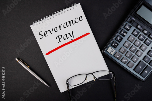 Fototapeta Naklejka Na Ścianę i Meble -  Text, the inscription, the phrase Severance Pay is written in a notebook that lies on a dark table with a calculator and pen and glasses. Business concept.