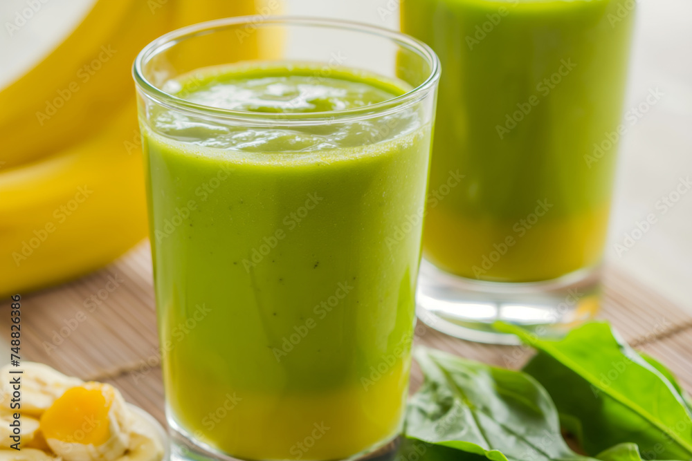 Two glasses of bright green smoothie, with bananas and spinach leaves on the side, representing a healthy lifestyle. Two glasses of bright green smoothie, with bananas and spinach leaves on the side, representing a healthy lifestyle.