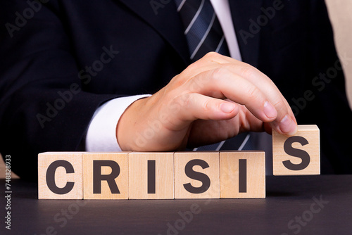 An American businessman is building the word Crisis from wooden building blocks. Business concept.