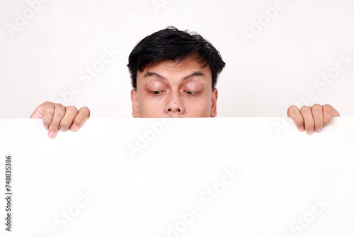 Portrait of young asian man standing behind an empty signboard and glancing on it