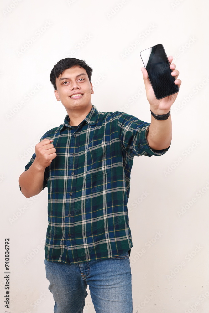 Happy young asian man showing a blank phone display with fist hand Happy young asian man showing a blank phone display with fist hand