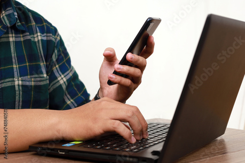 Close up photo of hand's man using a cell phone and a laptop. Technology concept