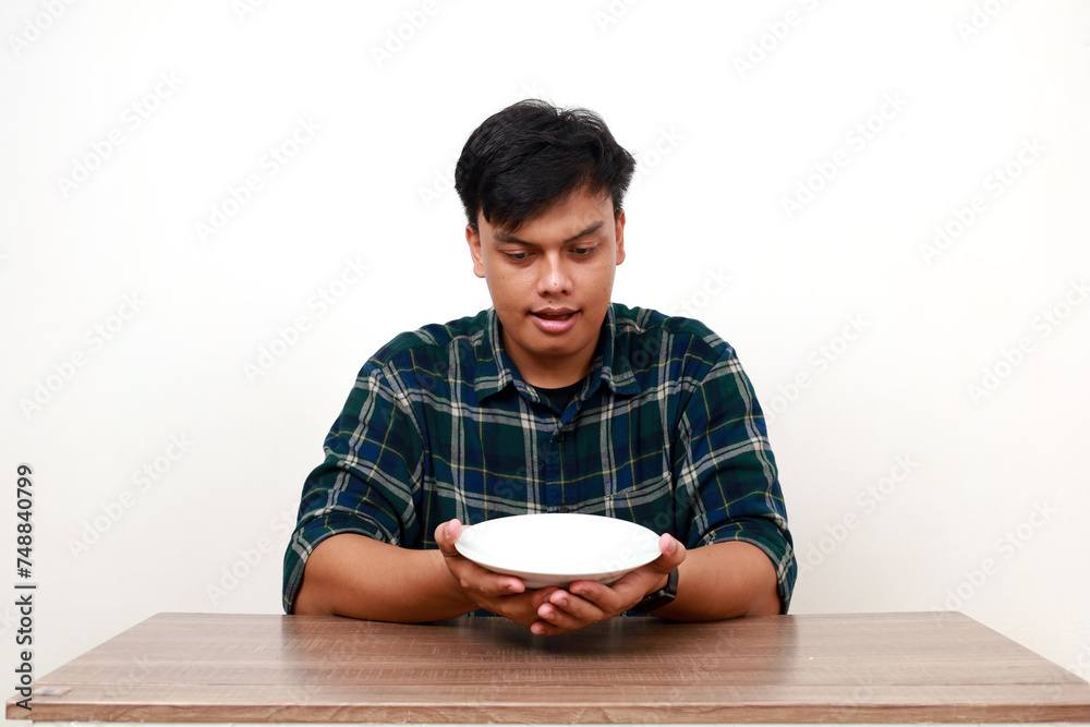Young asian man showing happy expression while holding an empty plate Young asian man showing happy expression while holding an empty plate