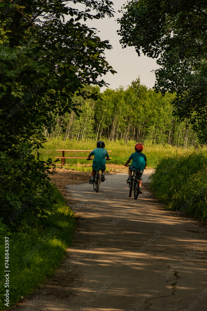 Boys riding  bikes on a bike  trail in the park through the trees.