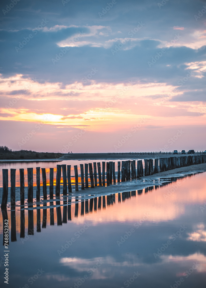 Lever du soleil et reflet dans l'eau de mer sur une plage en camargue avec des pêcheurs au loin et des poteaux en bois