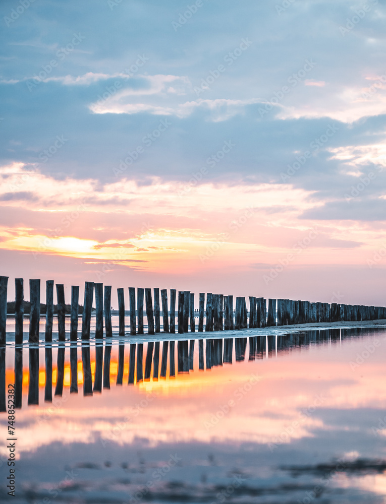 Lever du soleil et reflet dans l'eau de mer sur une plage en camargue avec des pêcheurs au loin et des poteaux en bois