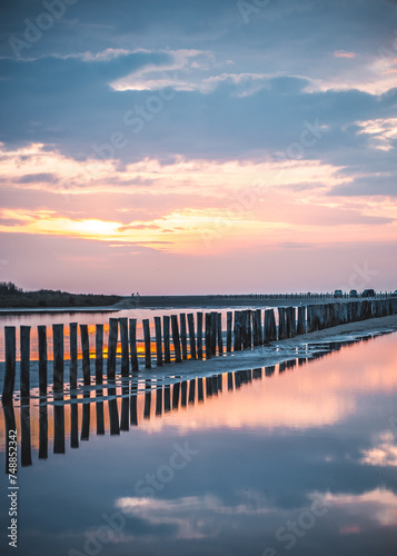 Obraz na płótnie Lever du soleil et reflet dans l'eau de mer sur une plage en camargue avec des pêcheurs au loin et des poteaux en bois w salonie