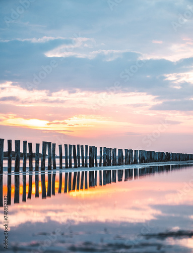 Obraz na płótnie Lever du soleil et reflet dans l'eau de mer sur une plage en camargue avec des pêcheurs au loin et des poteaux en bois w salonie