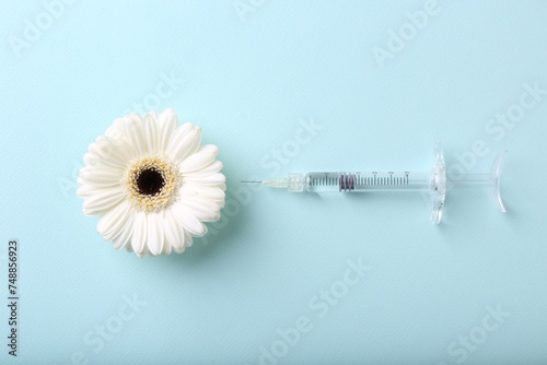 Cosmetology. Medical syringe and gerbera flower on light blue background, flat lay