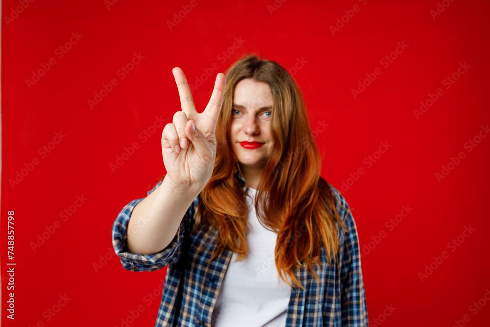 Cheerful 30s lady wearing checked shirt giving 2 sign isolated over bright red background, studio shoot. Hand showing two fingers Cheerful 30s lady wearing checked shirt giving 2 sign isolated over bright red background, studio shoot. Hand showing two fingers