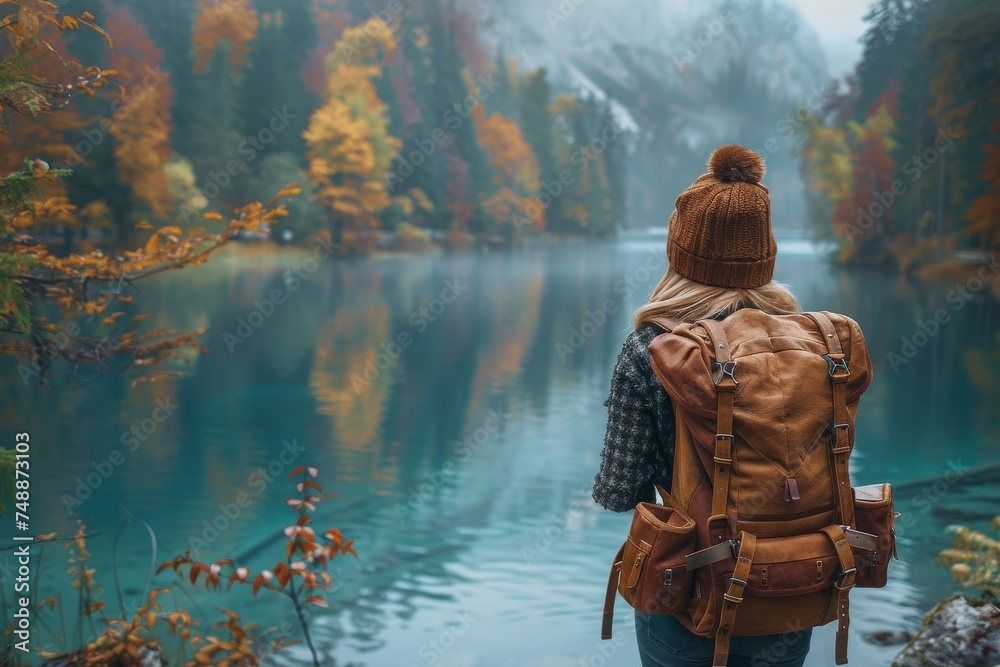 A peaceful capture of a woman with a backpack facing a calm lake surrounded by vibrant autumn foliage A peaceful capture of a woman with a backpack facing a calm lake surrounded by vibrant autumn foliage