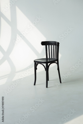 Chair with is an empty white room on a white background. There is a shadow on the wall from the window and the bright sun.