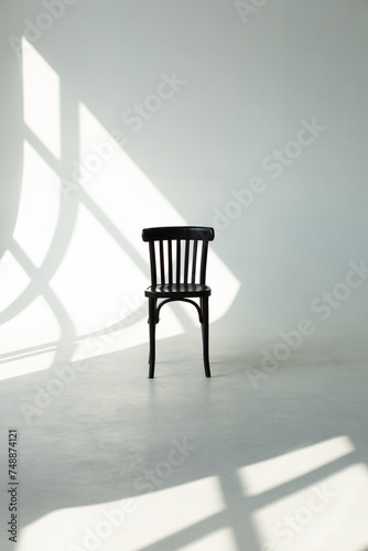 Chair with is an empty white room on a white background. There is a shadow on the wall from the window and the bright sun.