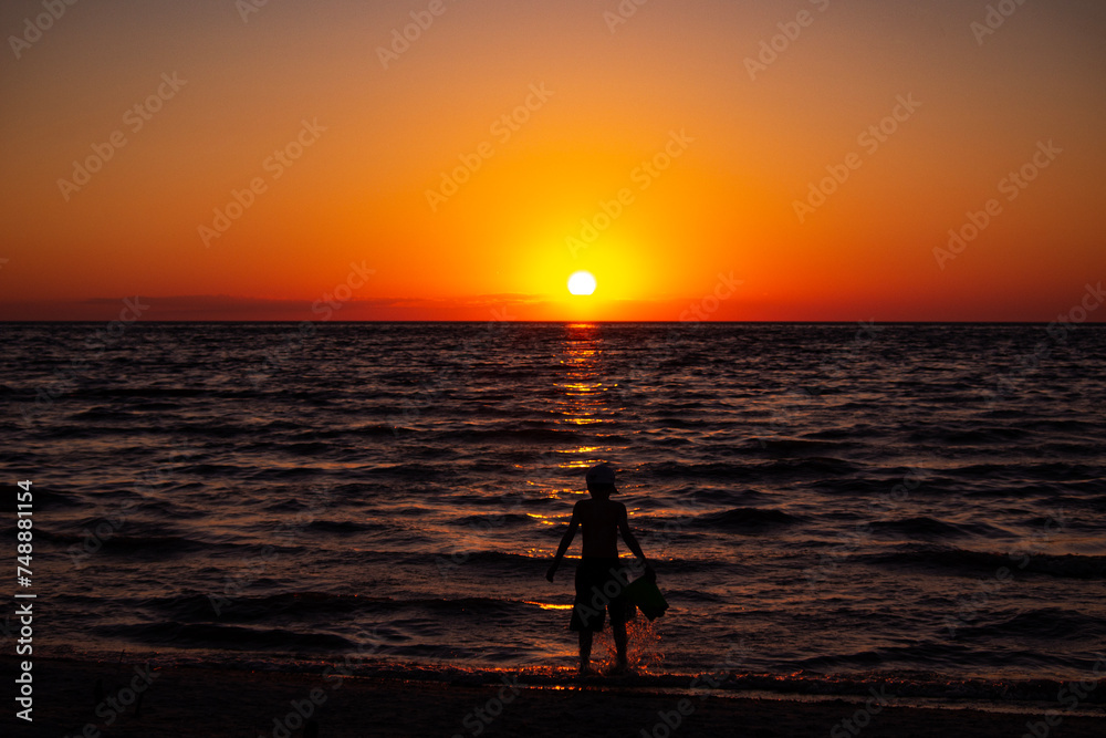 Silhouette of a boy on the beach at sunset.