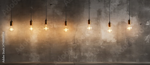 A group of light bulbs is hanging from the ceiling in a room with concrete walls and flooring. The light bulbs are illuminated, casting a bright glow in the space.