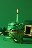 St. Patrick's day party. Tasty cupcake with burning candle and leprechaun hat on green background, closeup
