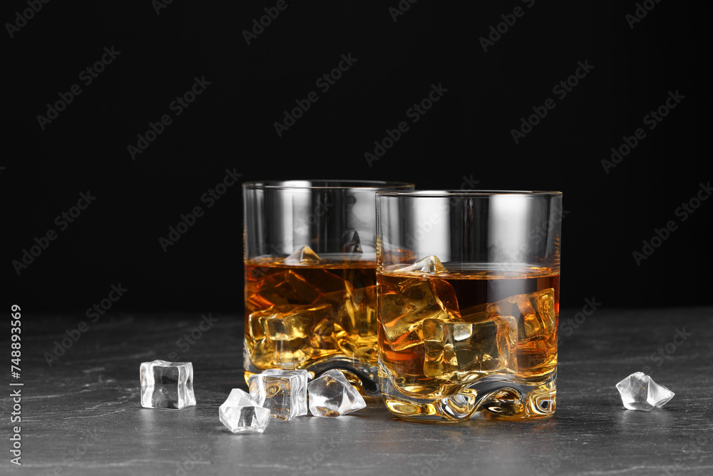 Whiskey and ice cubes in glasses on black table, closeup