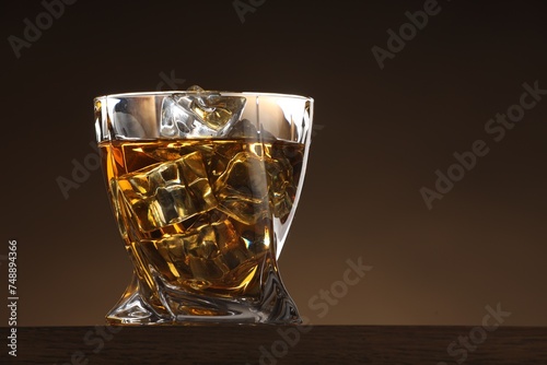 Whiskey with ice cubes in glass on table against brown background. Space for text