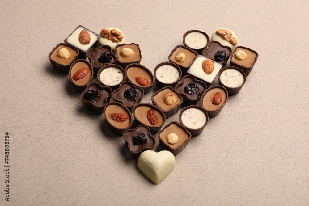 Heart made with delicious chocolate candies on beige background, above view Heart made with delicious chocolate candies on beige background, above view