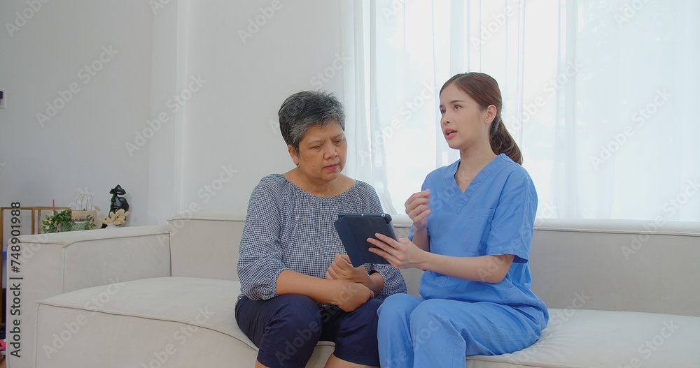 A healthcare professional in blue scrubs consults with an elderly patient using a tablet in a bright airy room A healthcare professional in blue scrubs consults with an elderly patient using a tablet in a bright airy room