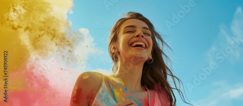 The image captures a young woman in a moment of jubilation, possibly during a color festival such as Holi. She has a broad smile on her face, enhancing the carefree and festive mood. Her hair and clot