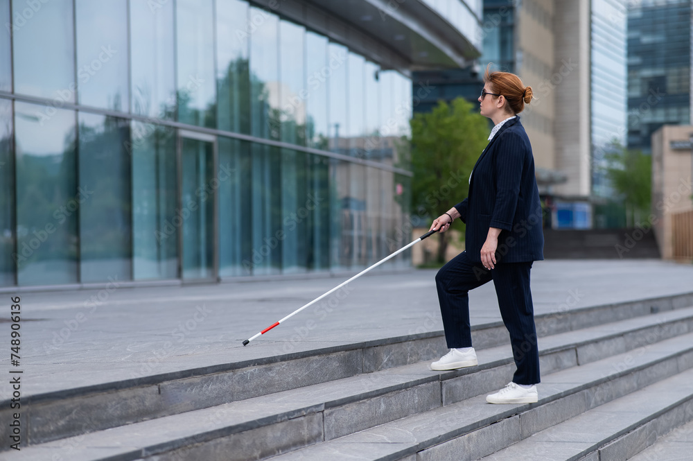 Blind business woman in glasses and with a cane climbs the stairs to the business center. 