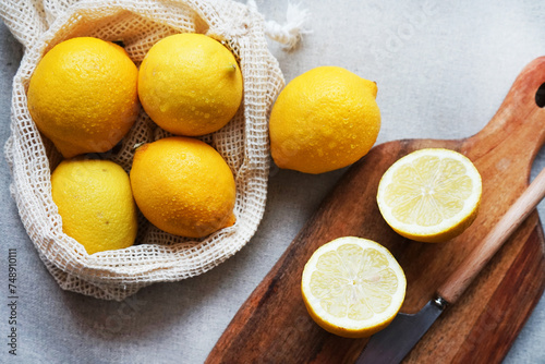 Whole and sliced ​​lemons on a wooden board next to a knife on a light background