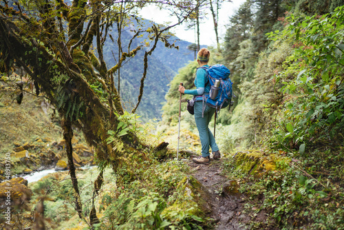 Young female with backpack and poles trekking walking Mera Peak climbing route through jungle rain forest in Makalu Barun National Park  Nepal. Active people and Himalayas tourism concept image.