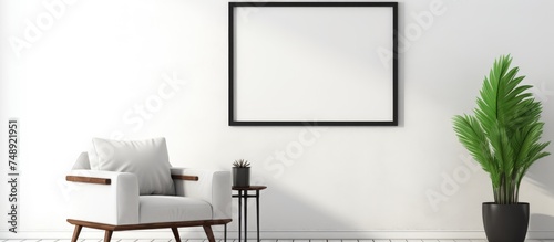 A contemporary living room features a chair and a potted plant. A blank black picture frame sits on a white shelf in the room.