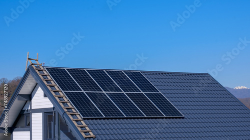 Solar panels on the roof of the house, against the blue sky. There is copy space