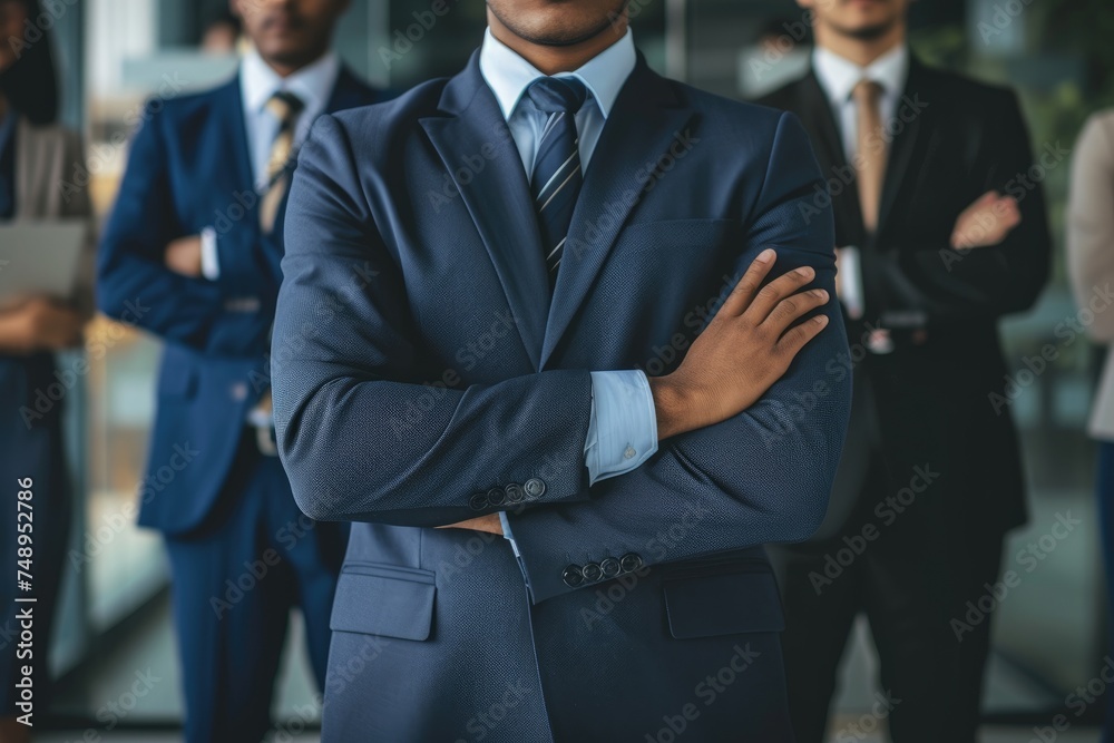 A confident business leader stands with crossed arms, exuding professionalism and leadership, as his team collaborates in the background. A confident business leader stands with crossed arms, exuding professionalism and leadership, as his team collaborates in the background.
