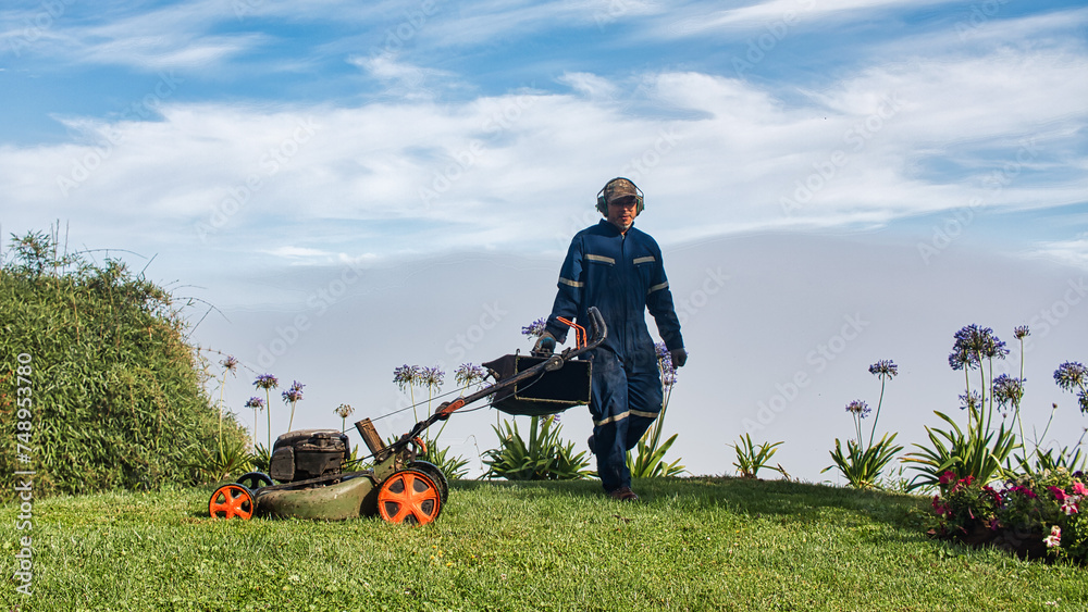 Yard worker mowing grass with lawn mower in garden. Lawn maintenance. Yard worker mowing grass with lawn mower in garden. Lawn maintenance.