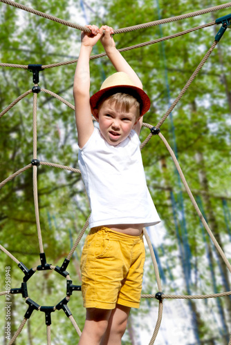 A child climbs up an alpine grid in a park on a playground on a hot summer day