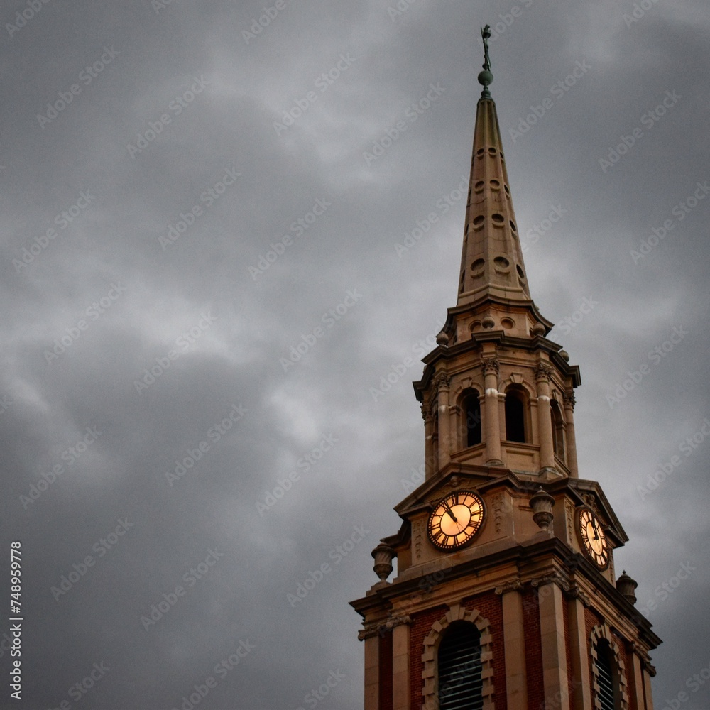 Gothic Church Steeple with Clock Tower Against Moody Overcast Sky at Dusk