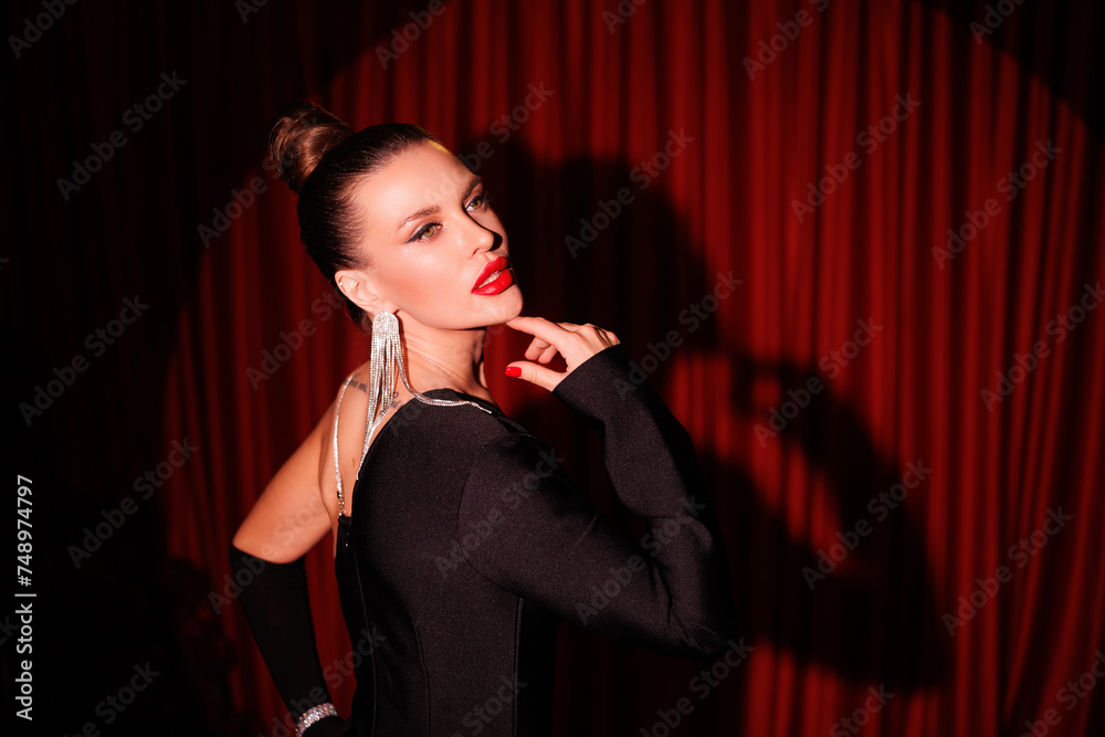 Gorgeous brunette woman in short black dress. Round light. Cabare style, St Valentines's Day. Beautiful lady with great make-up, big red lips, sparkling earrings portrait. Red curtains background Gorgeous brunette woman in short black dress. Round light. Cabare style, St Valentines's Day. Beautiful lady with great make-up, big red lips, sparkling earrings portrait. Red curtains background