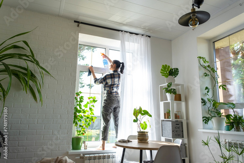 Woman manually washes the window of the house with a rag with spray cleaner and mop inside the interior with white curtains. Restoring order and cleanliness in the spring, cleaning servise