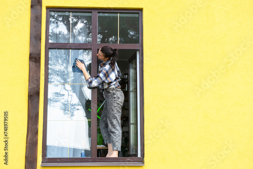 Wallpaper Mural A woman manually washes the window of the house with a rag with a spray cleaner and a mop outside. Safety at height, restoring order and cleanliness in the spring, cleaning service Torontodigital.ca