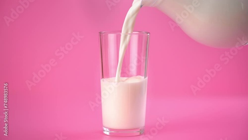 Glass and jug with milk in pink background, person pouring vegan plant milk, isolated studio shot