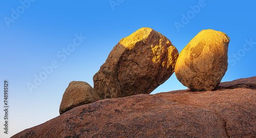 Three big rocks at the edge of rounded mountain at golden sunset light. Massive stones in a rock arch of Spitzkoppe, Namibia. Landscape with a balance of huge boulders at sky background.