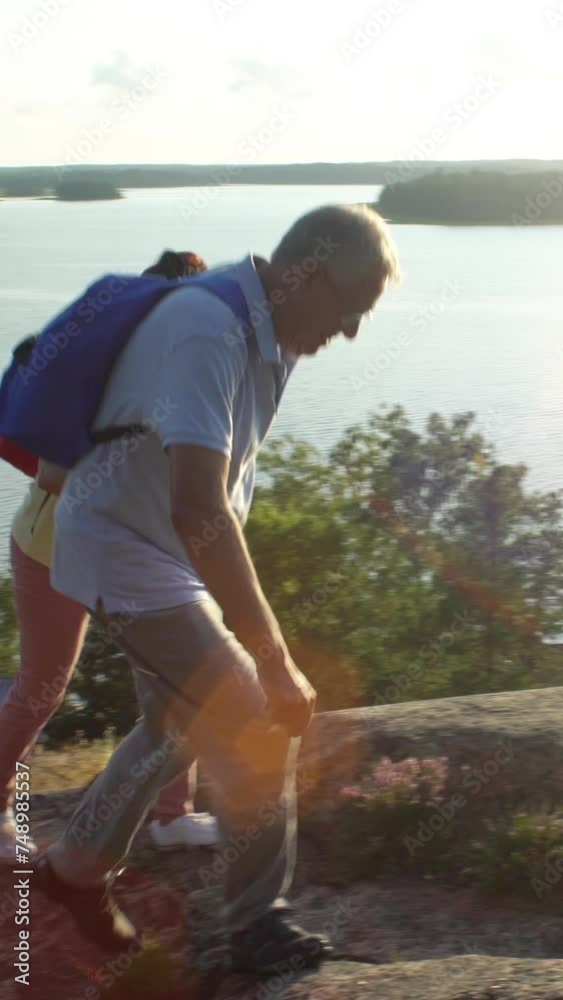 Elderly active couple climbing on the rock and admiring the sunrise, the sunset. Scandinavian landscape with sea and pine trees. Elderly active couple climbing on the rock and admiring the sunrise, the sunset. Scandinavian landscape with sea and pine trees.