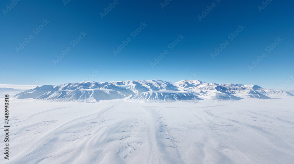 A serene aerial view of a mountain range covered in snow under a clear blue sky.