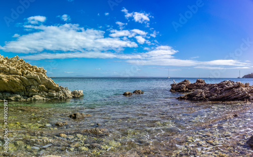 Rocky Coastal Inlet with Clear Shallow Waters and Sailing Boats under a Blue Sky © juanjo